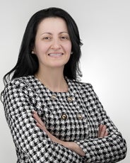 A woman with long black hair wears a black and white tweed jacket.