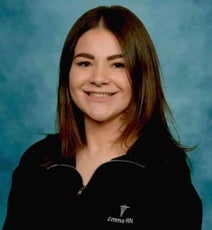 A woman with long brown hair wears a black zip-up sweater. 