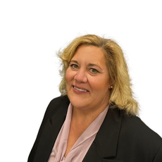 A woman with blonde hair wears a black suit jacket and light purple blouse.