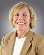 A woman with blonde hair wears a tan blazer and white top.