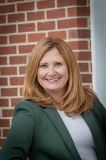 A woman with light hair wears a green jacket over a white shirt.