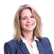 A woman with shoulder-length blonde hair wears a blue blazer and white striped button down