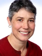 A headshot of a woman with short grey hair who is wearing a red sweater