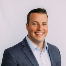 A headshot of a man with short hair wearing a suit jacket and button down shirt