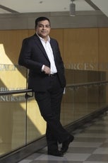 Parth Chakrabarti, executive vice chancellor at UMass Chan, dressed in a blue suit and black shoes with a white shirt and no tie, leans against a railing. 