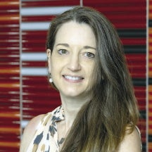 A woman with brown hair stands in front of a red background.