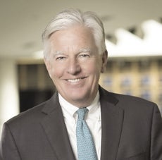 A headshot of a man with white hair, a black suit jacket, white button down, and light blue tie