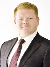 A headshot photo of a man with red hair wearing a suit