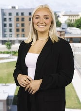 A woman with blonde hair wears a black blazer and white top.