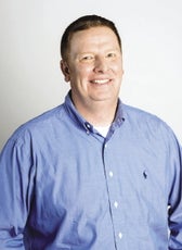 A man smiles while wearing a blue button-up shirt