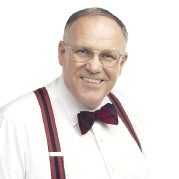 A man with glasses wears a white shirt with suspenders and a bow tie.
