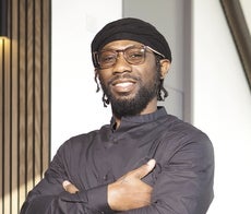 A man in a portrait photo with his arms crossed, wearing glasses and a hat