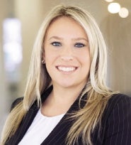 A woman with blond hair wears a black jacket.