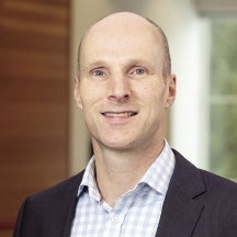 A man with a dark jacket and striped shirt smiles for the camera.