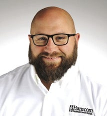 A man with a brown beard and glasses wears a white shirt.