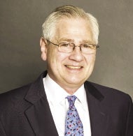 A man with glasses wears a purple tie, white shirt, and black jacket.