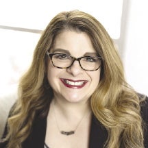 A woman with glasses wears a black blazer