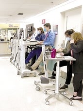 Physicians at UMass Memorial in front of a nursing station using computers on wheeled tables
