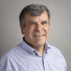 A man with black and gray hair is wearing a blue and white striped shirt.