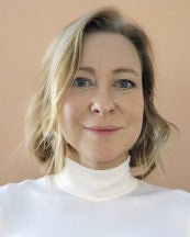A woman with blonde hair wears a white sweater.