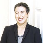 A woman in a black suit and gray shirt smiles at the camera.