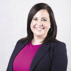 A woman with shoulder-length straight, dark brown hair wears a black blazer and purple top.