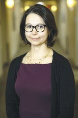A woman with short, straight black hair wears a black cardigan and dark purple top.