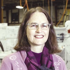 A woman with glasses and brown hair wears a purple outfit