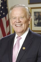 man in suit smiling with U.S. flag in the background