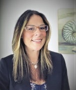 A woman with long hair is wearing glasses and a black jacket.