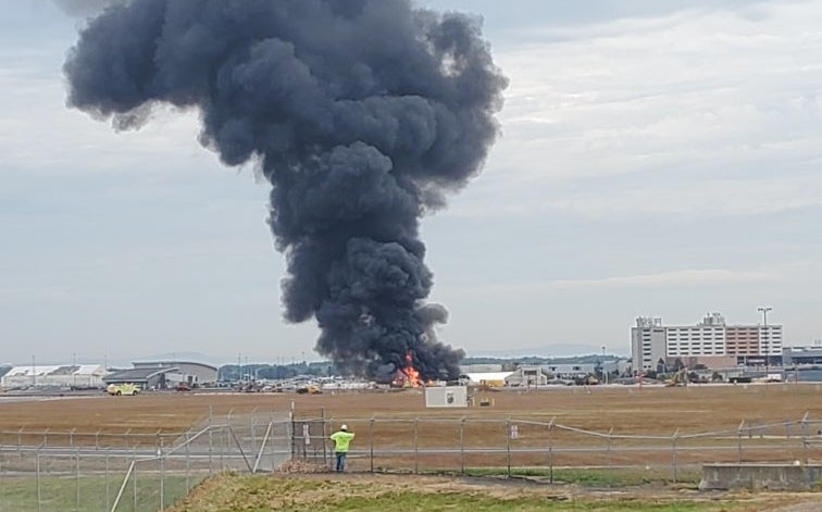 A pillar of smoke rises out of the flaming wreckage of an airplane at a Connecticut airport.