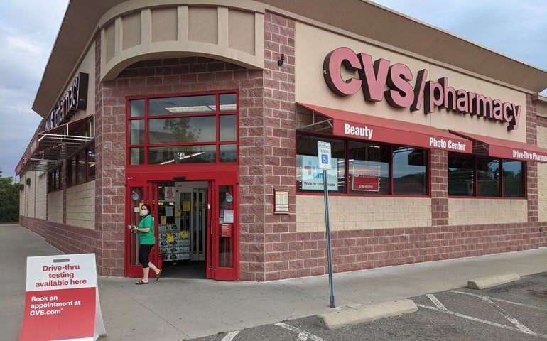 A large brick building with "CVS/pharmacy" printed in large red letters on the side sits behind a parking lot.