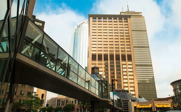 A cluster of three tall buildings behind an outdoor glass walkway.