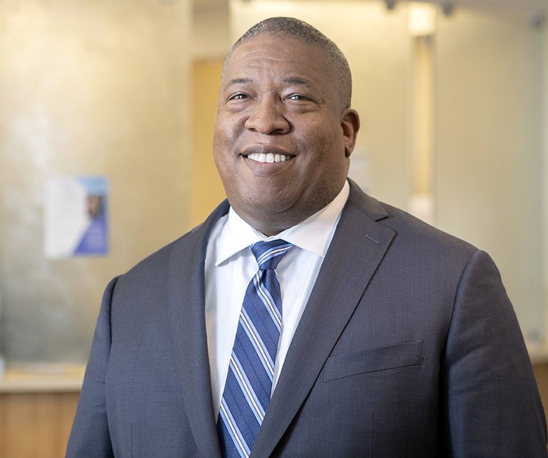 A man wears a blue suit with a blue-striped tie.