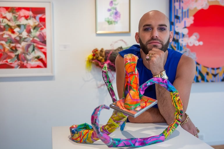 Joshua Croke poses behind a multicolor sculpture.