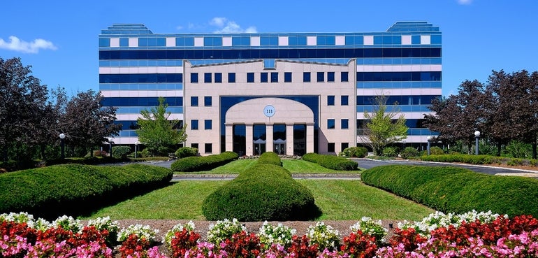 A large windowed building sits behind two grass plots with pink, red, and white flowers in the foreground