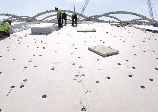 Workers on a white roof work to add panels to the roof