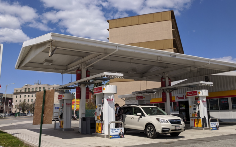 A gas station with four pumps under an awning with a white van parked underneath.