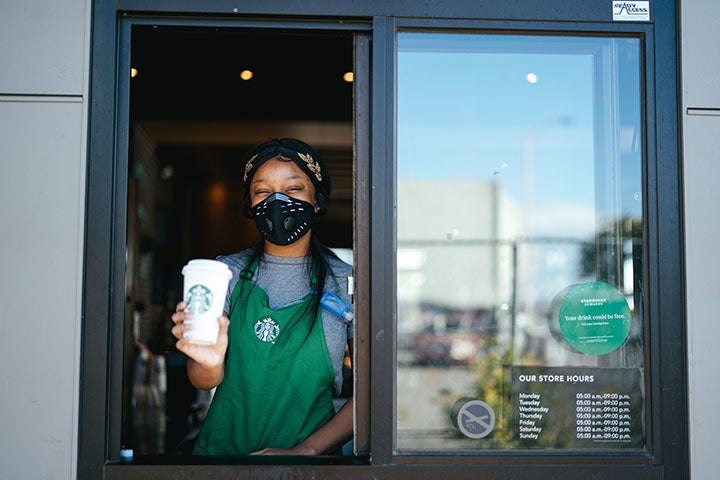 Photo of Starbucks barista at drive thru window handing coffee to viewer