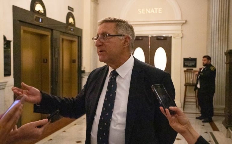 Man in suit answers questions to reporters in the state house