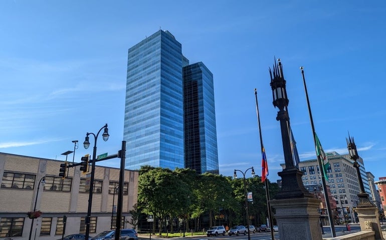 A large blue skyscraper sits behind trees
