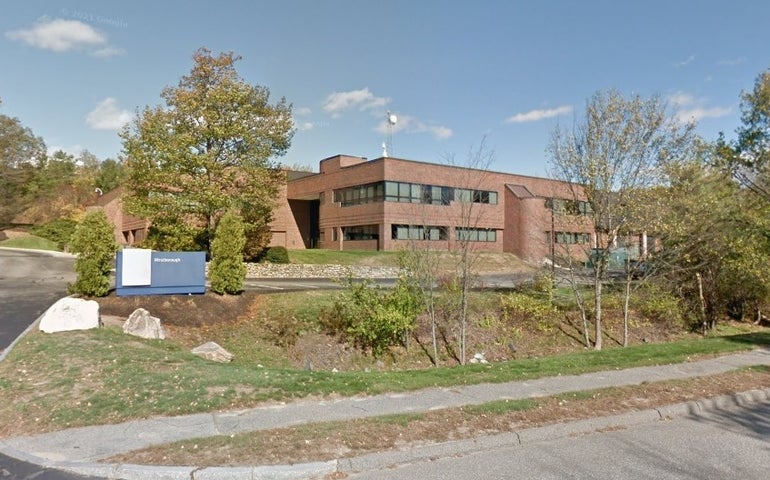 A brown multi-story building surrounded by trees and roads.