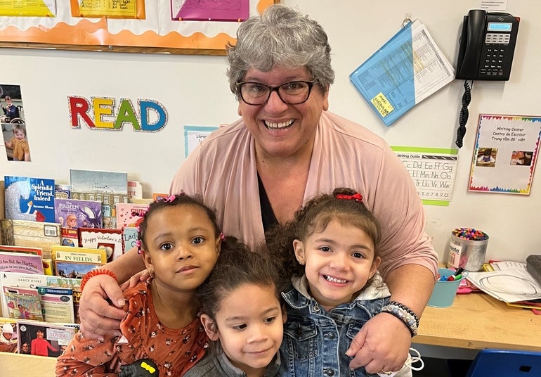 Edward Street master teacher Jo Ann Borinski hugs three children in a classroom at the YWCA Central Massachusetts.