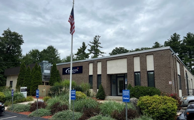 A brick building with greenery in the foreground and a US flag atop a pole