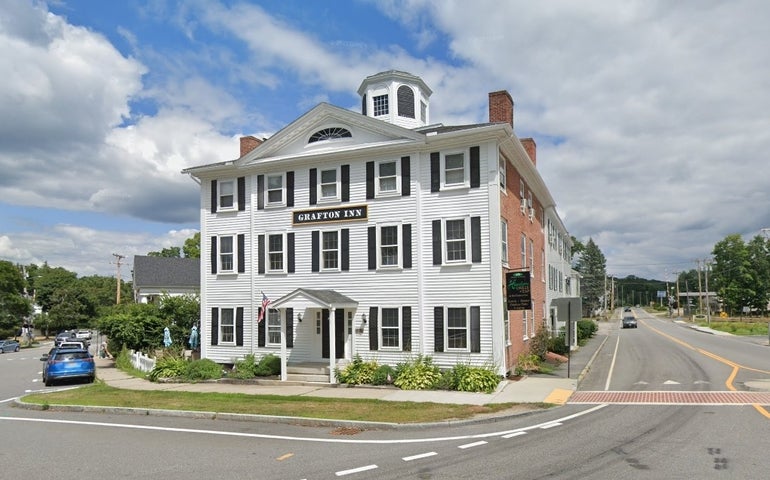 A three story white-sided and brick building with a cupola on top, bearing the name Grafton Inn