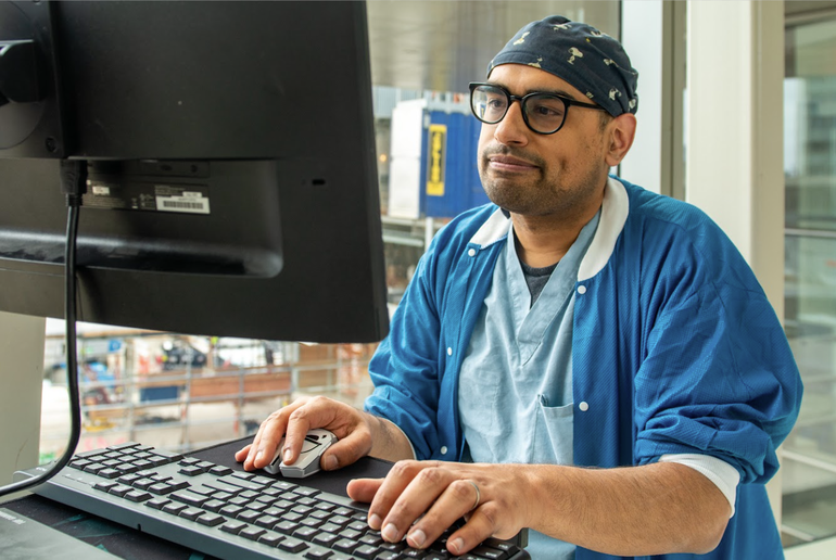 Dr. Marya wearing surgical attire using a desktop computer.