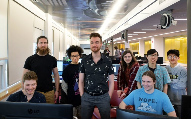 A group of students line up behind computer monitors