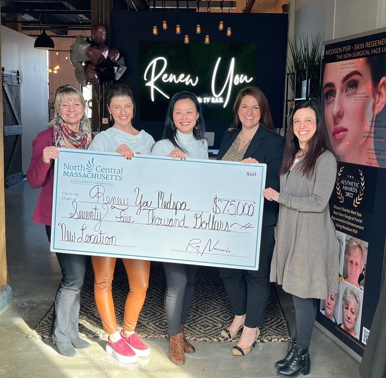 Five women stand in the front of spa, holding a giant check representing a $75,000 loan.
