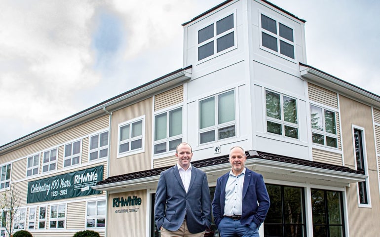 Two men in sports jackets stan in front of a ruilding with a sign that reads RH White 41 Central Street and has a banner celebrating its 100th year in operation