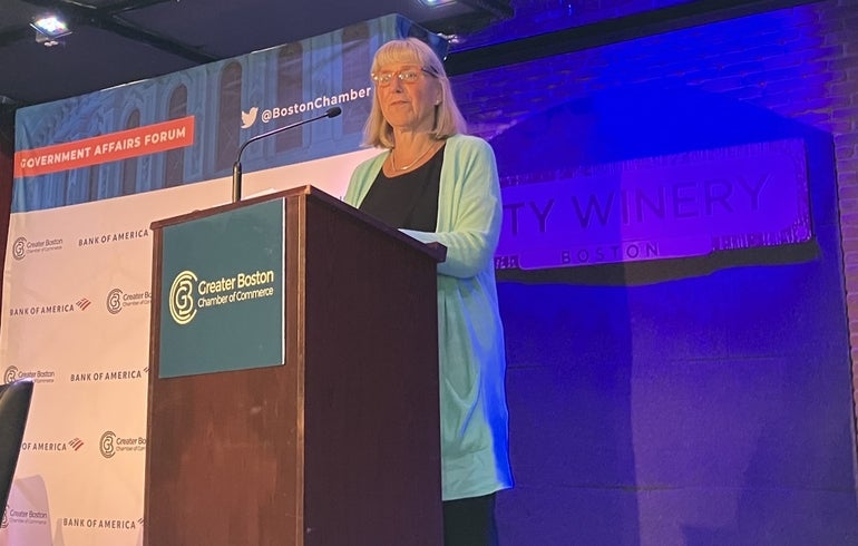 A white woman with bangs and red glasses behind a podium that says Greater Boston Chamber of Commerce